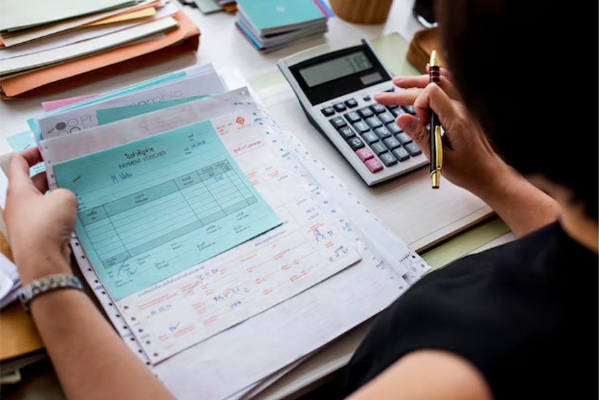 Person calculating finances with calculator and paperwork.